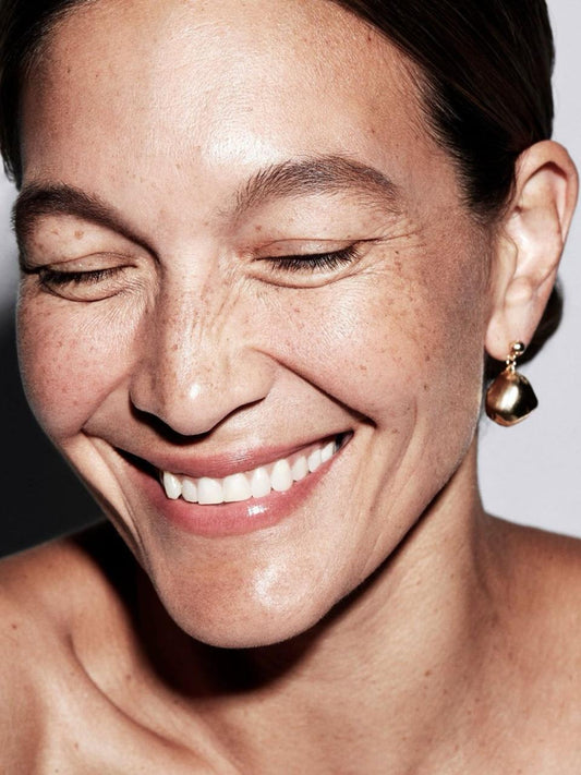 Close-up of a woman's face with a neutral expression on a gray background for AGE-DEFENCE ROUTINE – Skin Renewal Routine Kit.